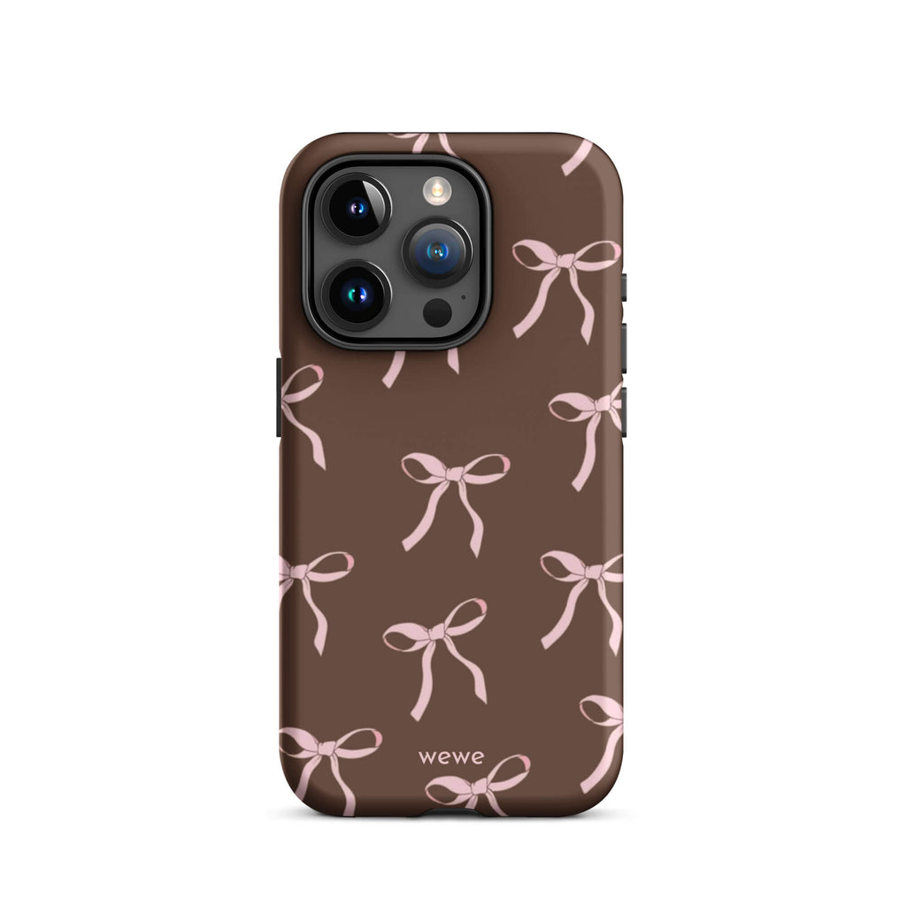 Custom iPhone 15 pro tough case in matte dark brown (chocolate) featuring an all-over repeating pattern of light pink ribbons/bows, with 'wewe' branding at the bottom.
